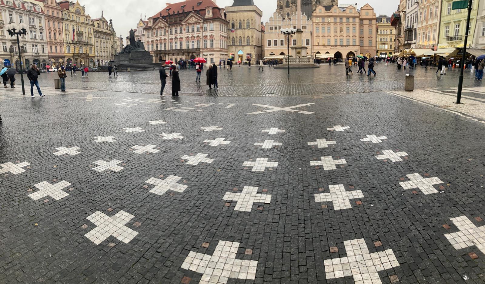 Weiße Kreuz-Mahnmale im Kopfsteinpflaster eines historischen Stadtplatzes.