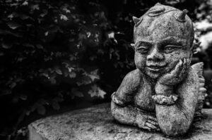 A small stone statue of a smiling cherub resting its head on its hand.