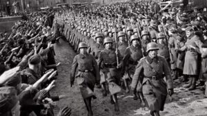 Black-and-white photo of German soldiers marching as crowds salute on both sides.