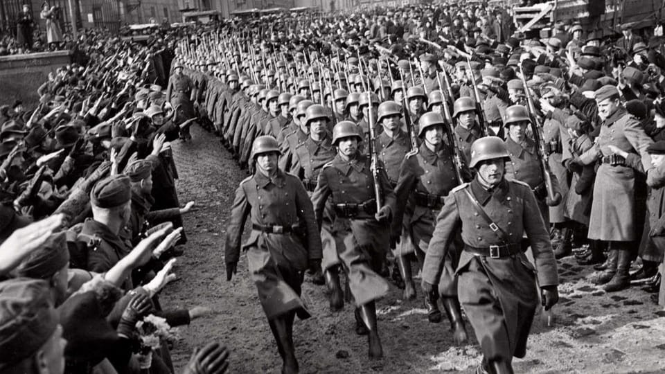 Black-and-white photo of German soldiers marching as crowds salute on both sides.